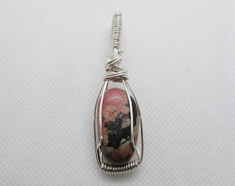 May include: A silver wire wrapped pendant featuring a pink and black oval shaped gemstone.