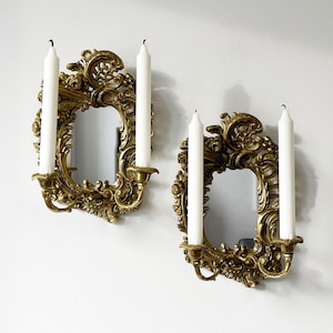 May include: Two ornate gold wall sconces with mirrored centers and two white candles each.