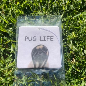 Pu&ograve; includere: Un profumatore per auto bianco con un'immagine di un carlino in bianco e nero e la scritta "PUG LIFE" stampata su di esso.