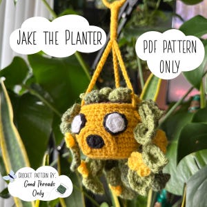 Puede incluir: Una maceta colgante de ganchillo amarilla hecha a mano con forma de personaje de dibujos animados, con ojos blancos y nariz negra. La maceta tiene detalles verdes y está suspendida por un cordón amarillo. El texto de la imagen dice "Jake the Planter" y "PDF Pattern Only".