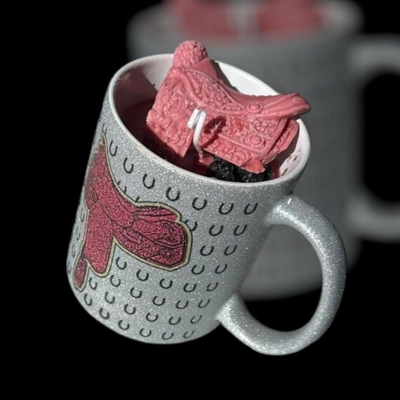 Western saddle on a shimmering pink coffee cup with inspirational quotes on opposite side. Pink swirl with horse head profiled can be custom