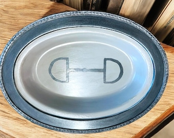 Può includere: Un piatto da portata ovale argentato con un bordo nero e un design a staffa argentato al centro.