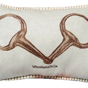 May include: A white pillow with a brown leather horse bit design. The pillow has a white background and a brown border. The text "ThePillowPaddock.Etsy.com" is printed on the bottom of the pillow.