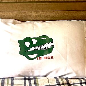 May include: White pillowcase with a green dinosaur skull graphic and the text "PAUL MICHAEL" printed in red.
