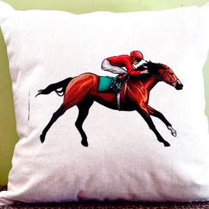 May include: A white throw pillow with a colorful illustration of a jockey riding a brown horse. The horse is in mid-stride, and the jockey is wearing a red and white uniform.