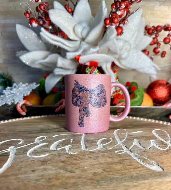 Western saddle on a shimmering pink coffee cup with inspirational quotes on opposite side. Pink swirl with horse head profiled can be custom