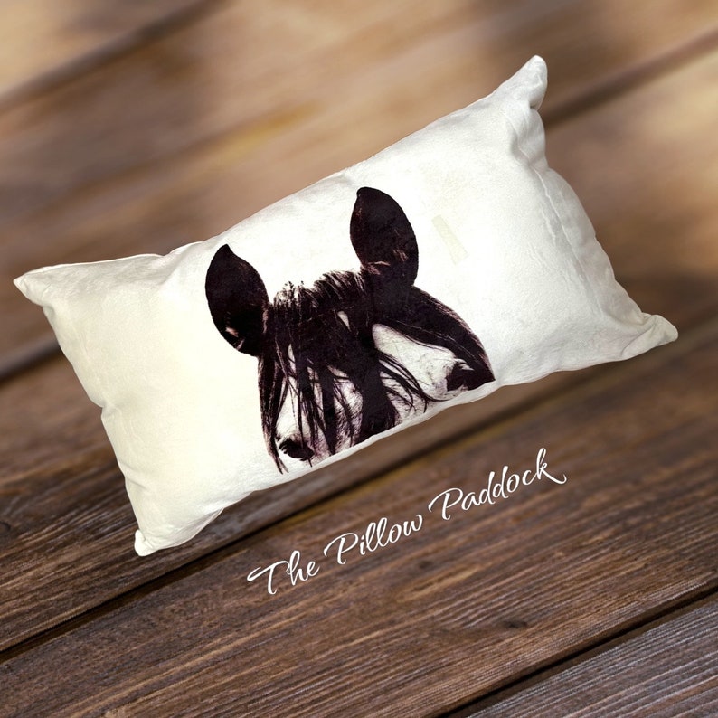 Pu&ograve; includere: Un cuscino bianco con la testa di un cavallo bianco e nero stampata su di esso. Il cuscino ha il testo "The Pillow Paddock" stampato sul fondo.