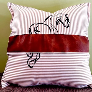 May include: A brown and white striped pillow with a brown leather band and a black silhouette of a horse.