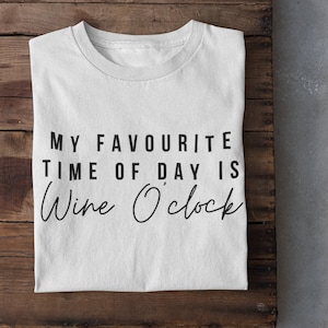 Puede incluir: Camiseta blanca con texto negro que dice "My favorite time of day is Wine O'clock".