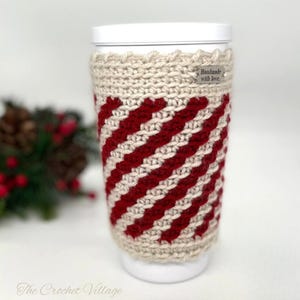 May include: A crocheted coffee cup cozy with a red and beige striped pattern. The cozy has a small metal tag that says "Handmade with love."