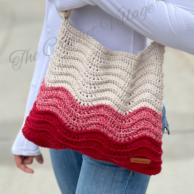 May include: A crocheted tote bag with a wavy pattern in beige, pink, and red. The bag has a wooden handle and a leather tag that says "Knit Made".