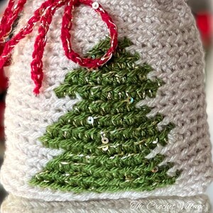 May include: A close-up of a crocheted Christmas stocking with a green and gold sequined Christmas tree design. The stocking is white with a red ribbon.