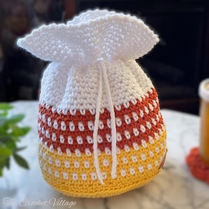 Puede incluir: Bolsa de cordón de maíz dulce de crochet blanco con rayas naranja, blancas y amarillas.