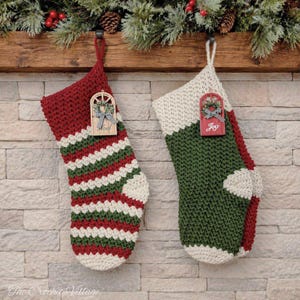 Puede incluir: Dos calcetines de Navidad hechos a mano. Uno es rojo con rayas verdes y blancas, el otro es verde con un talón y puño rojos. Ambos tienen un adorno de madera con una corona y un lazo. Los calcetines cuelgan de una viga de madera.