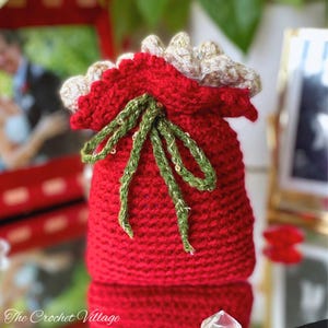May include: A red crocheted gift bag with a green and gold ribbon. The bag is decorated with gold sequins.