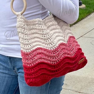 May include: A crocheted tote bag with a wooden handle. The bag is made with a cream and red yarn and has a wavy pattern.