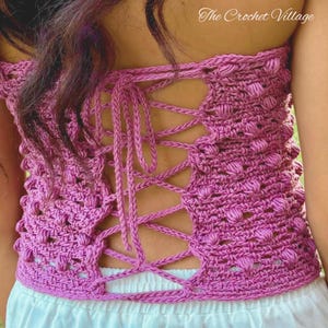 May include: A pink crocheted top with a lace-up back. The top is made with a textured stitch and has a slightly puffy appearance.