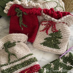 May include: Four crocheted Christmas stocking ornaments in red, beige, and green with gold glitter accents. The ornaments are decorated with a green Christmas tree design and a red bow.