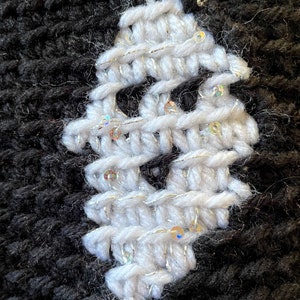 May include: A close-up of a white knitted fabric with silver sequins. The fabric is stitched onto a black knitted fabric.