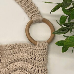 May include: A beige crocheted bag with a wooden ring handle. The bag has a textured, woven design.