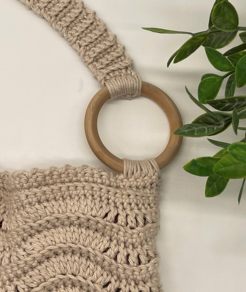 May include: A beige crocheted bag with a wooden ring handle. The bag has a textured, woven design.