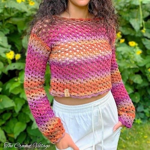 May include: A long-sleeve crochet top featuring a variegated color pattern of pink, orange, and purple hues. The garment has a loose, open-knit stitch design, a round neckline, and a small rectangular tan label attached to the bottom hem.