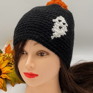 May include: Black crocheted beanie with a white ghost design and an orange pom pom on top.