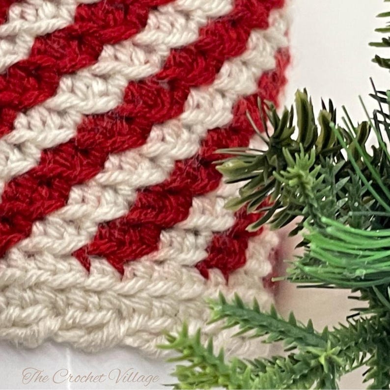 May include: Close-up of a crocheted red and white striped ornament. The ornament is made with a textured stitch and has a diagonal pattern.