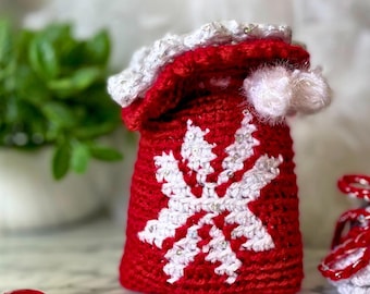 Könnte beinhalten: Ein roter, gehäkelter Weihnachtssocken mit einem weißen Schneeflockenmuster und einem weißen Bommel oben.