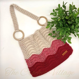 May include: A crocheted tote bag with a wavy pattern in beige, pink, and red. The bag has two wooden handles and a small leather tag that says "Knit Goods".
