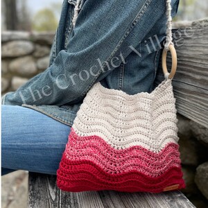 May include: A crocheted tote bag with a wavy pattern in beige and red. The bag has a wooden ring handle and is worn over the shoulder.