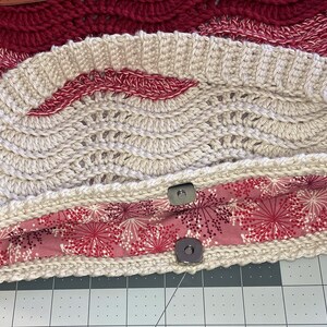 May include: A beige crocheted bag with a red and white patterned fabric lining. The bag has two wooden handles and two metal snaps.