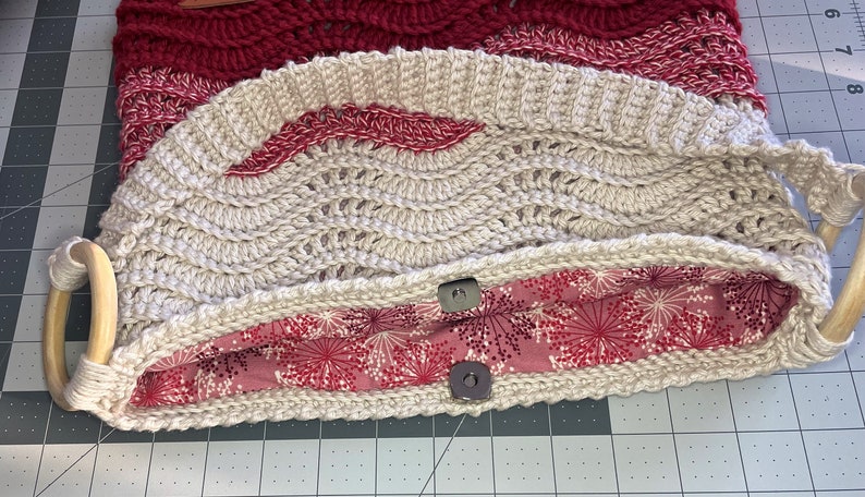 May include: A beige crocheted bag with a red and white patterned fabric lining. The bag has two wooden handles and two metal snaps.