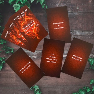 Puede incluir: Un juego de cartas de or&aacute;culo con fondo rojo y naranja. Las cartas presentan frases como "Silent Heart Love Oracle", "Twin Flame Journey", "I'm Done Playing Games", "Mental Health", "Passion & Desire", y "Andromeda Skies".