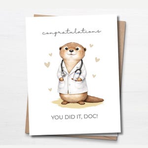 May include: A greeting card with a cartoon otter in a white lab coat and stethoscope. The card says "congratulations" and "YOU DID IT, DOC!" with heart illustrations. The card is on a brown envelope.