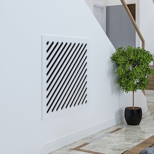 May include: A white wall with a black and white geometric design on a square panel. A small green potted plant is on the floor next to the wall.