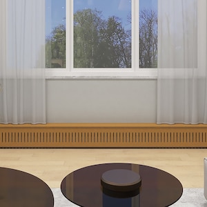 May include: A wooden radiator cover with a slatted design, installed beneath a window with white curtains. The cover is a light brown color and is situated in a room with a light wood floor and two round glass coffee tables.
