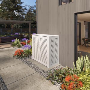 May include: White outdoor air conditioning unit with a slatted cover, installed on the side of a house with a gray siding. The unit is surrounded by landscaping with green bushes and flowers.