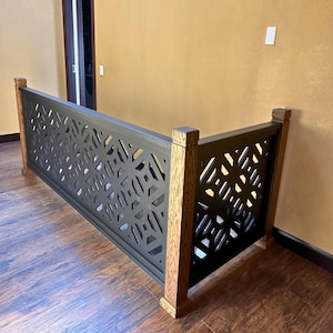 May include: A custom-built, decorative railing with a geometric pattern. The railing features a dark gray metal panel with cut-out designs, framed by natural wood posts and a top rail. The design adds a modern touch to the interior space.