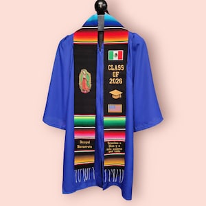May include: A royal blue graduation gown with a black sash. The sash features the text "CLASS OF 2026", a Mexican flag, a graduation cap, and an American flag. The sash also has the text "Danyel Navarrete" and "Gracias a Dios y a mis padres por todo".