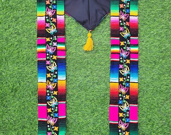 May include: A graduation stole with a pink, black, green, blue, yellow, and orange striped pattern. The stole has a black background with embroidered butterflies and flowers in various colors. The stole has a yellow tassel.
