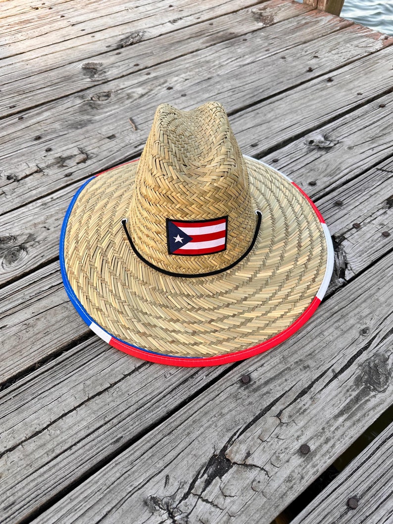 May include: A straw hat with a red, white, and blue trim and a Puerto Rican flag patch. The hat is sitting on a wooden surface.
