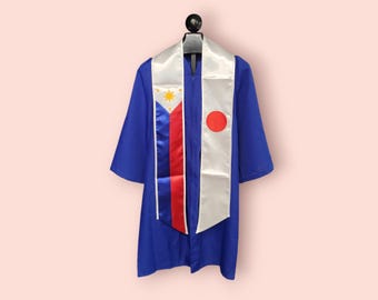 May include: A blue graduation gown with a white and red sash featuring the flag of the Philippines and a white sash with a red circle, representing the flag of Japan.