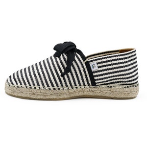 May include: Black and white striped espadrille shoes with black ribbon laces. The shoes have a jute sole.