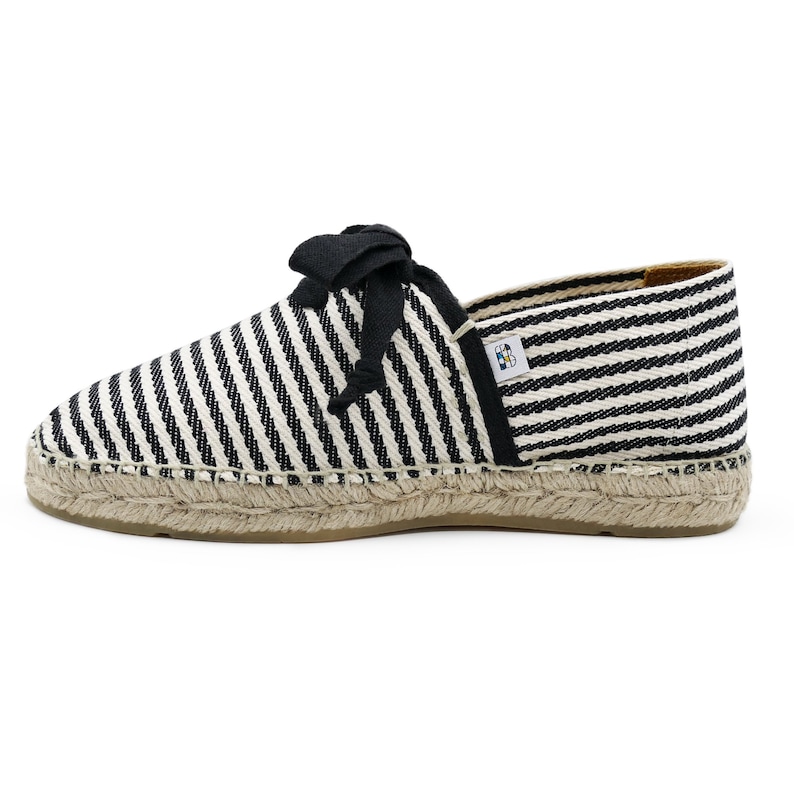 May include: Black and white striped espadrille shoes with black ribbon laces. The shoes have a jute sole.