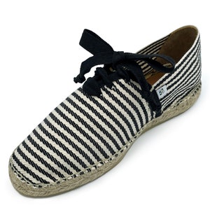 May include: Black and white striped espadrille shoes with black laces. The shoes have a jute sole and a label that says "BB".