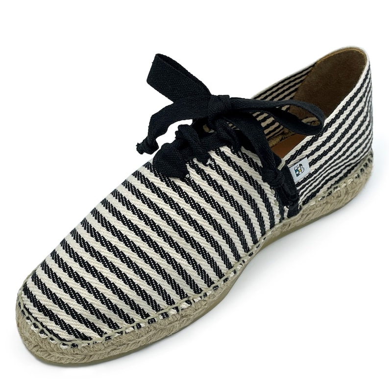 May include: Black and white striped espadrille shoes with black laces. The shoes have a jute sole and a label that says "BB".