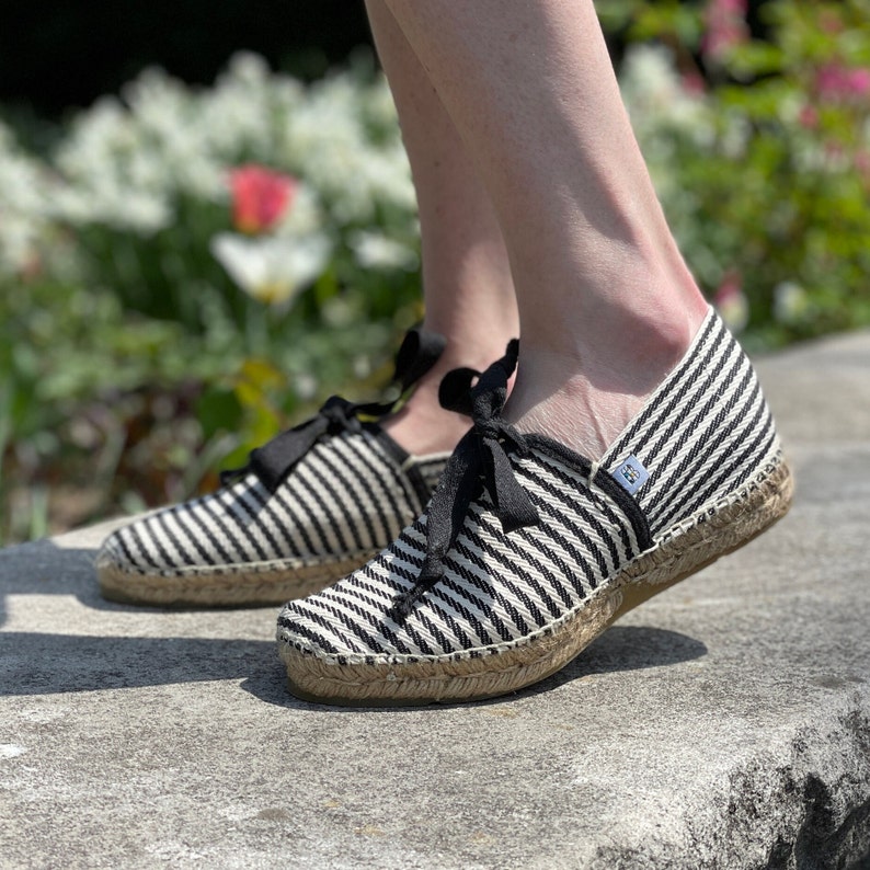 May include: A pair of black and white striped espadrille shoes with black laces. The shoes are made of canvas and have a jute sole.