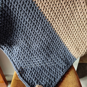 K&ouml;nnte beinhalten: Eine blaue und braune geh&auml;kelte Decke mit einer Blumenverzierung. Die Decke ist mit einem strukturierten Stich gearbeitet und hat einen diagonalen Farbwechsel.