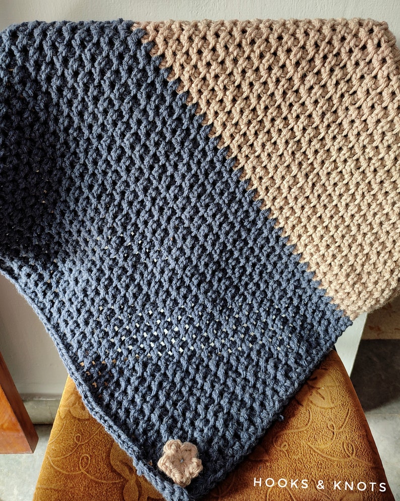 K&ouml;nnte beinhalten: Eine blaue und braune geh&auml;kelte Decke mit einer Blumenverzierung. Die Decke ist mit einem strukturierten Stich gearbeitet und hat einen diagonalen Farbwechsel.